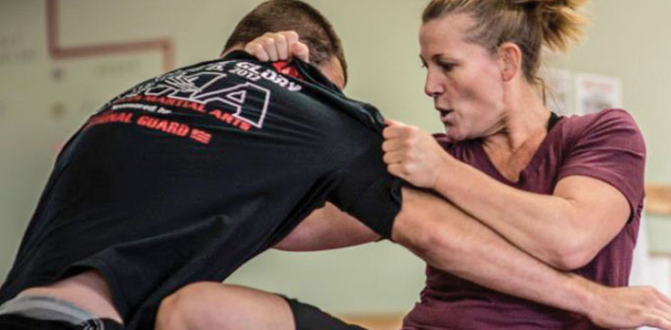 Female Krav Maga black belt student throwing a knee strike to a man's midsection. Man doubled over in pain