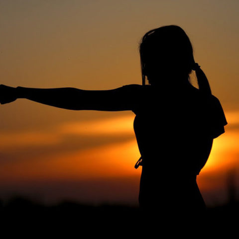 Silhouette of woman punching set against the background of a setting sun.